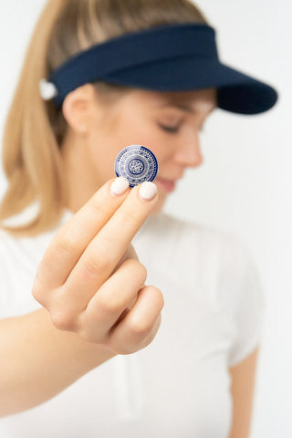 Navy ladies golf visor constructed with quick-drying fabrics. The visor comes in a one size fits all design with an elasticated cord at the rear to hold it securely in place. It also features a concealed magnet  in peak with a hand enamelled lace golf ball marker attached, making it a lovely golf accessory, golf gift! The headband features a soft lined absorbent towel. 